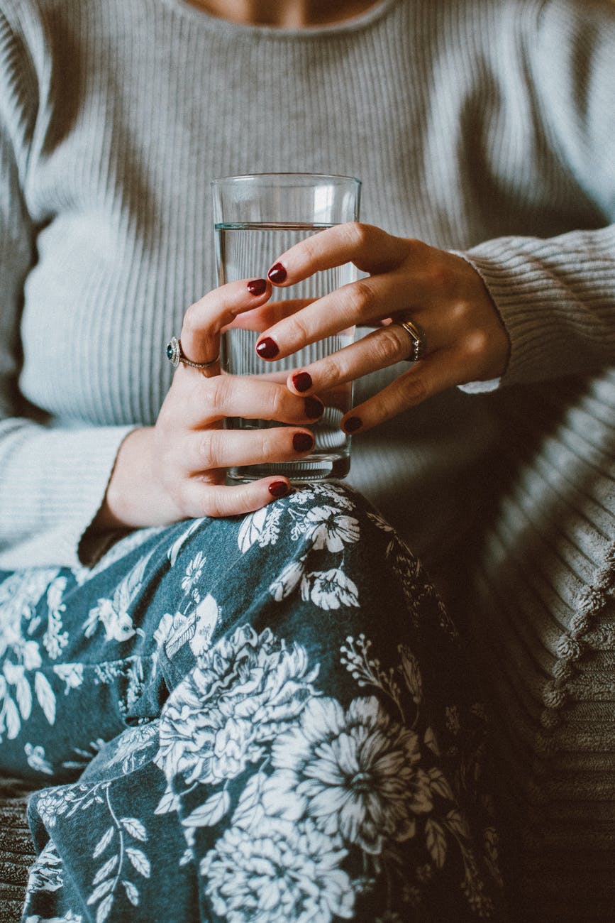 person sitting on grey sofa while holding clear highball glass of water