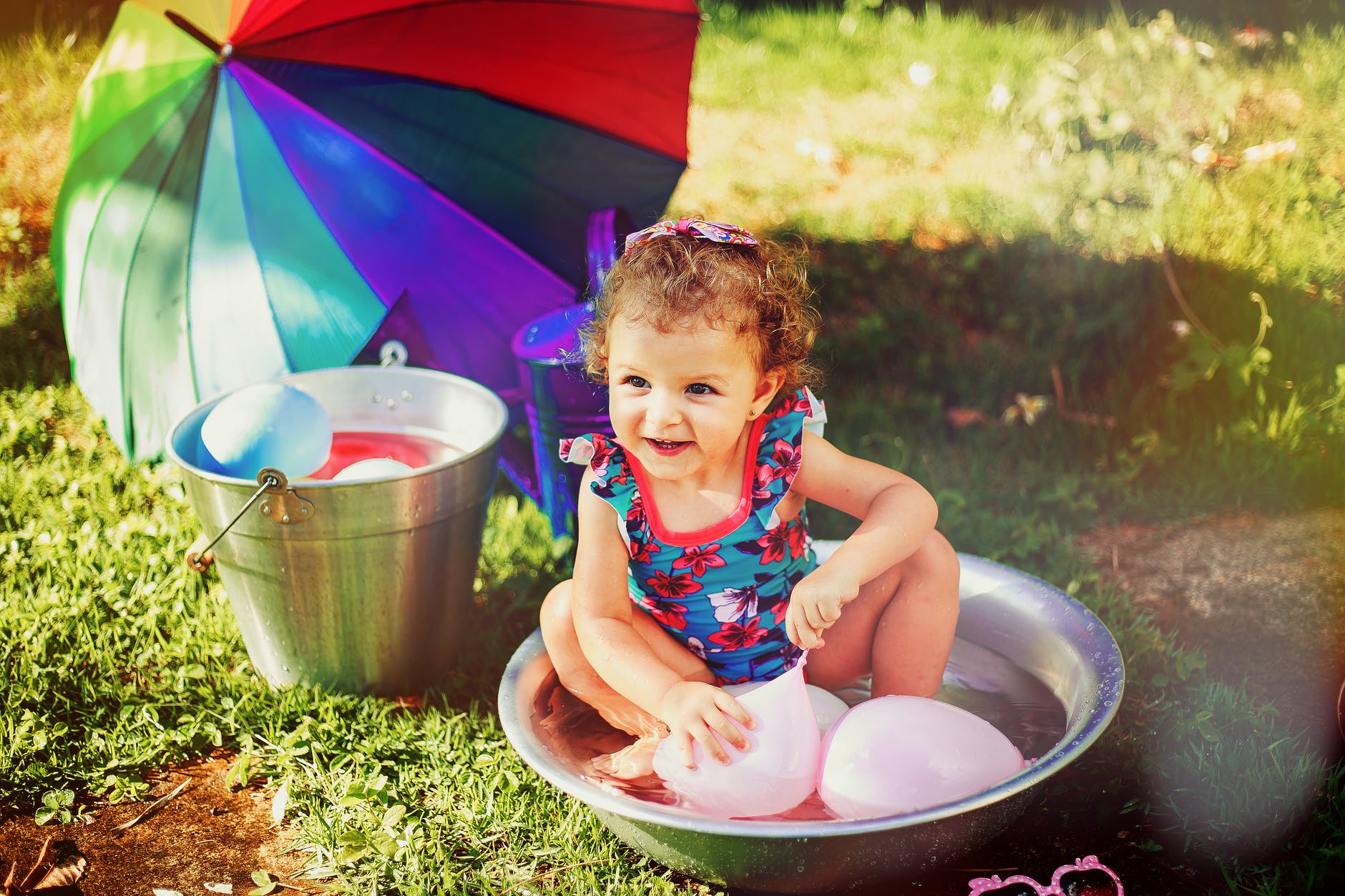 smiling girl sitting on gray stainless steel basin playing with pink balloons