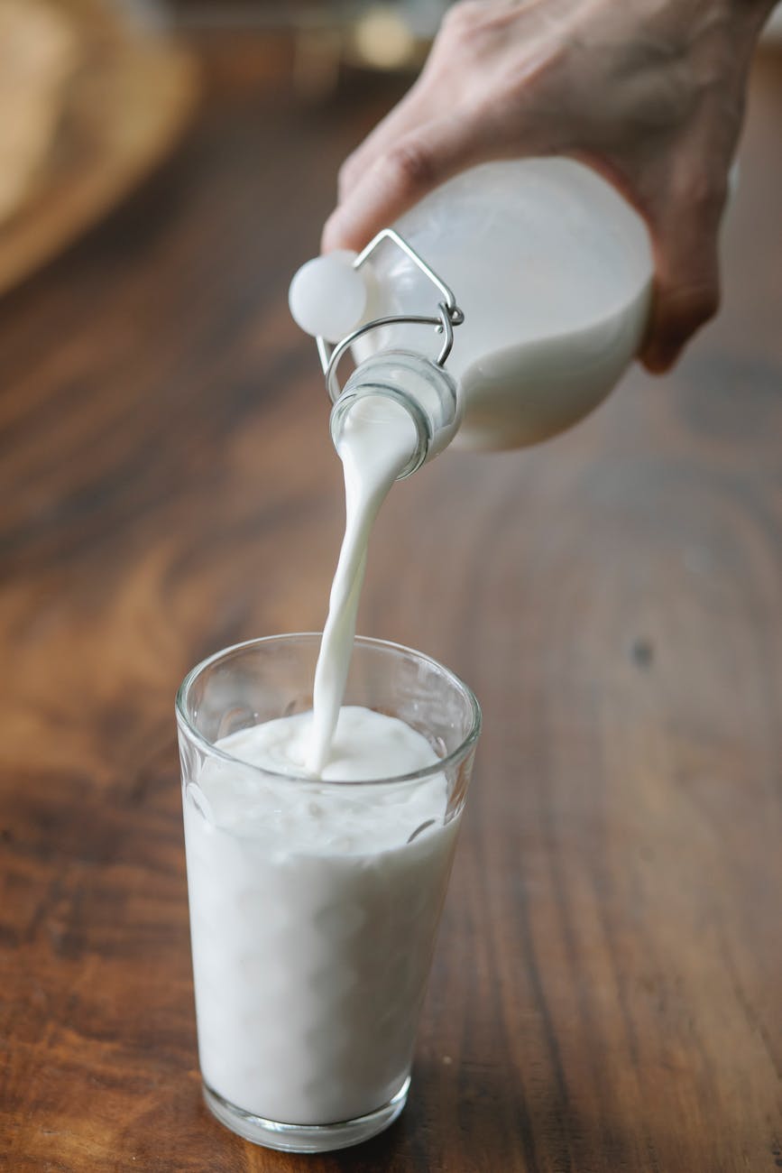 crop person pouring milk into glass on table