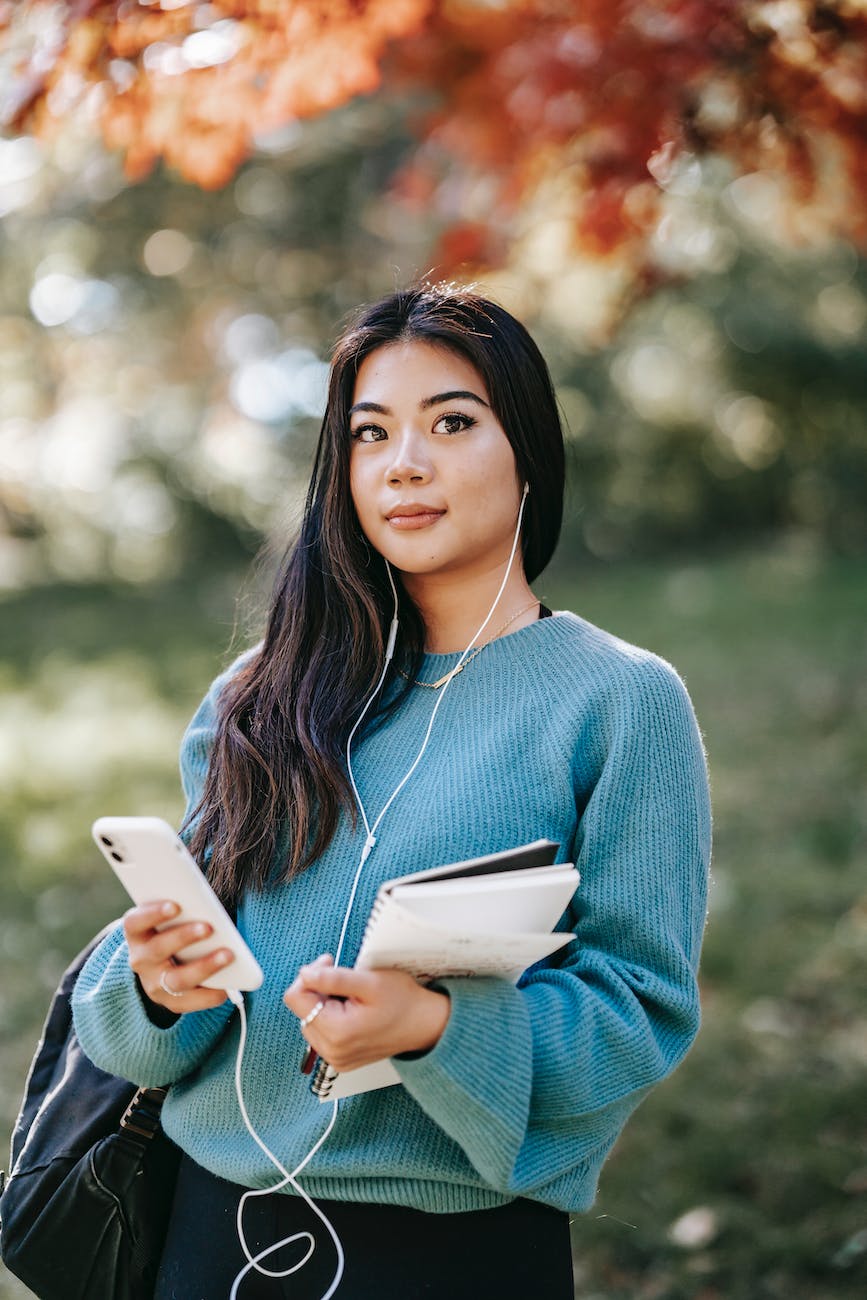 asian woman with notebook listening to music with smartphone and earphones
